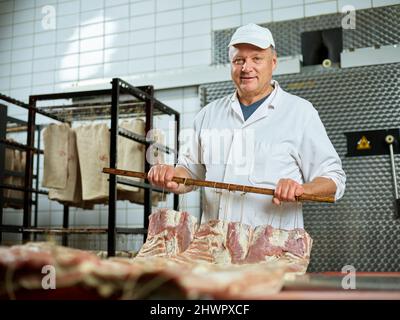 Smiling butcher with fresh raw meat standing in factory Stock Photo