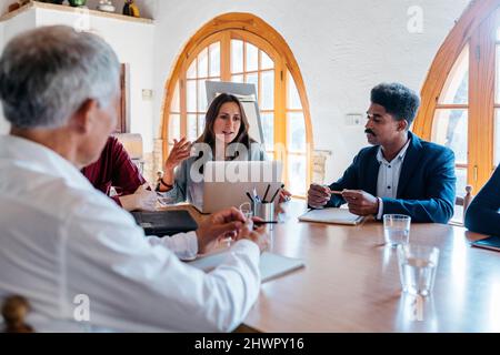 Businesswoman using laptop and discussing with colleagues in meeting room Stock Photo