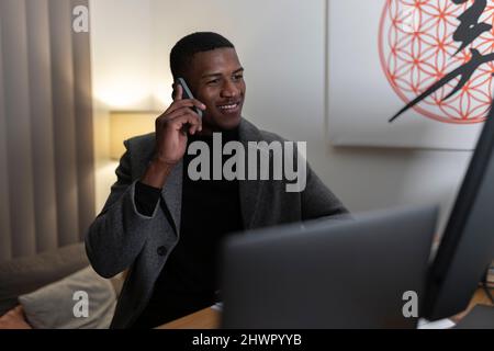 Smiling young businessman talking on mobile phone at home working late night Stock Photo