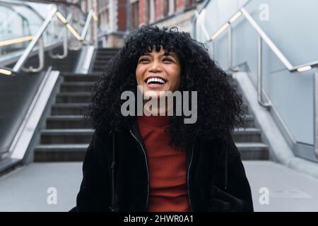 Happy young curly haired woman in front of staircase Stock Photo