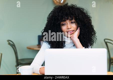 Curly black haired woman using laptop at cafe Stock Photo