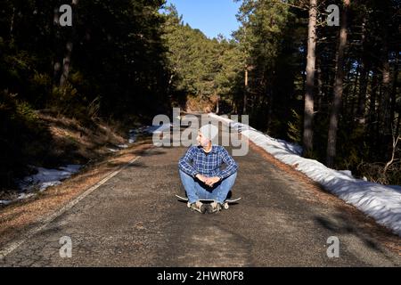 Man wearing knit hat sitting on skateboard Stock Photo