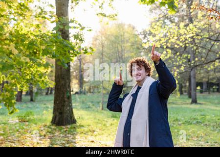 Smiling young man with curly red hair and scarf dancing in autumn park Stock Photo