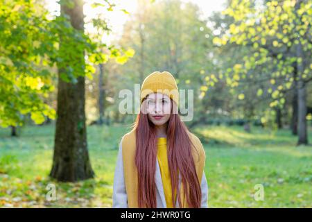 Redhead woman wearing yellow knit hat and scarf standing in autumn park Stock Photo