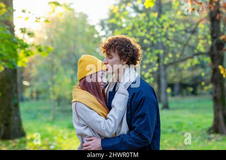 Young man embracing and kissing girlfriend's forehead in autumn park Stock Photo