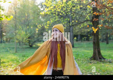 Smiling redhead woman wearing yellow knit hat and scarf day dreaming in autumn park Stock Photo