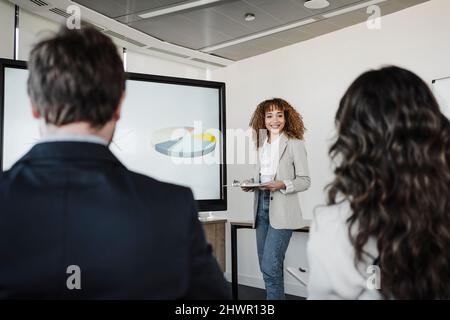 Smiling young businesswoman giving presentation to colleagues in board room Stock Photo