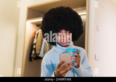 Smiling woman using mobile phone and having coffee in bedroom Stock Photo