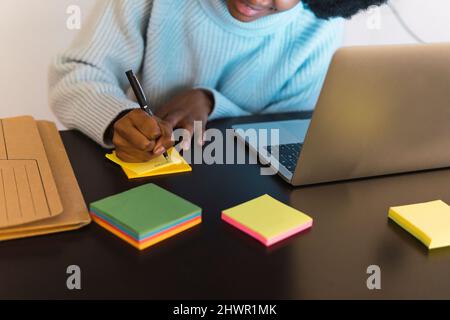 Freelancer writing on adhesive note by laptop at home Stock Photo