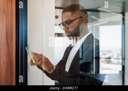 Businessman sticking adhesive note on glass wall at office Stock Photo