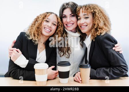Young businesswoman embracing colleagues at coffee break in coworking office Stock Photo