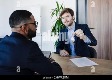 Real estate agent holding house keys talking to client in office Stock Photo