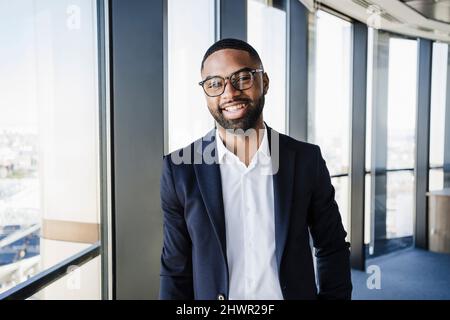 Happy businessman leaning on window in office Stock Photo