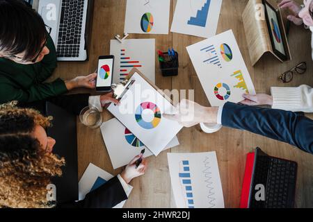 Business colleagues discussing over pie chart at desk in coworking office Stock Photo