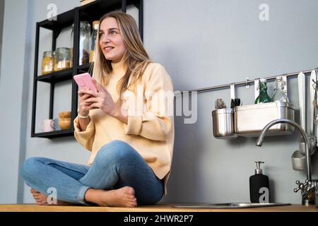 Contemplative woman with smart phone in kitchen Stock Photo