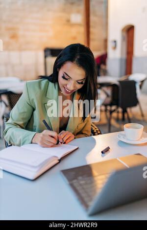 Young freelancer writing in diary at cafe Stock Photo
