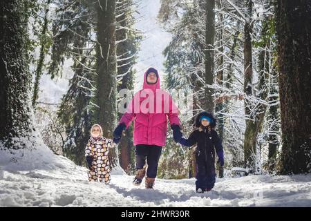 Father with daughters walking in snowy forest on sunny day Stock Photo