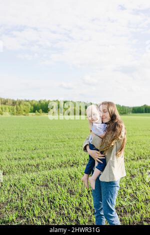 Mother with eyes closed hugging son at green field Stock Photo