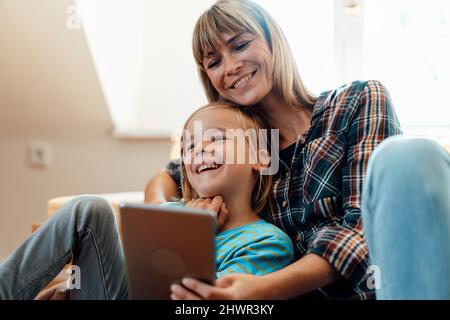 Son laughing by mother using tablet PC at home Stock Photo