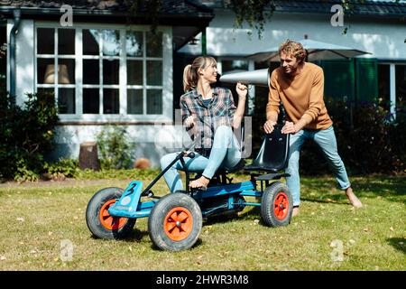 Man pushing woman on go-cart talking through megaphone in garden Stock Photo
