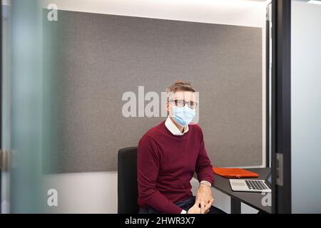 Businessman wearing protective face mask sitting on chair at office Stock Photo