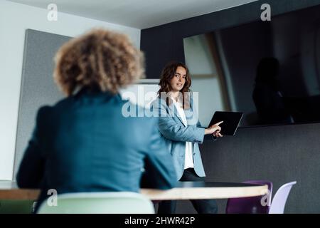 Businesswoman pointing on tablet PC giving presentation to colleague in board room Stock Photo