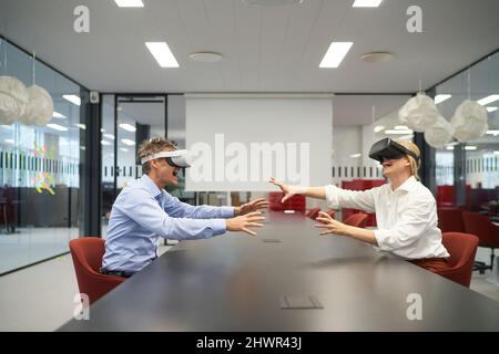 Colleagues using VR glasses sitting at conference table in office Stock Photo