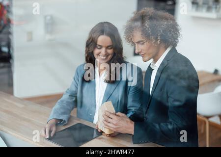 Smiling businessman with tablet PC standing by colleague explaining model house in office Stock Photo
