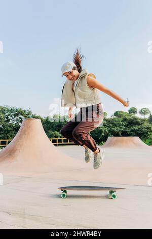 Smiling woman jumping over skateboard in park Stock Photo