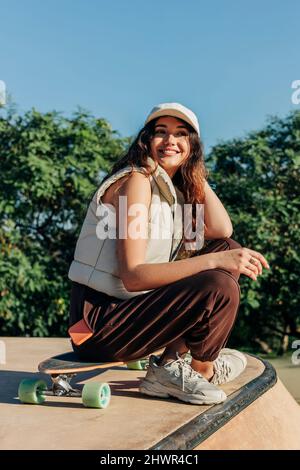 Young woman day dreaming on skateboard in park Stock Photo