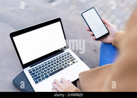 Woman with laptop text messaging through smart phone Stock Photo