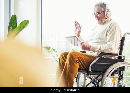 Smiling disabled man waving hand on video call through tablet PC at home Stock Photo
