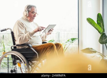 Senior disabled man using tablet PC on wheelchair at home Stock Photo