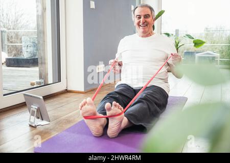 Happy senior man with resistance band doing workout at home Stock Photo