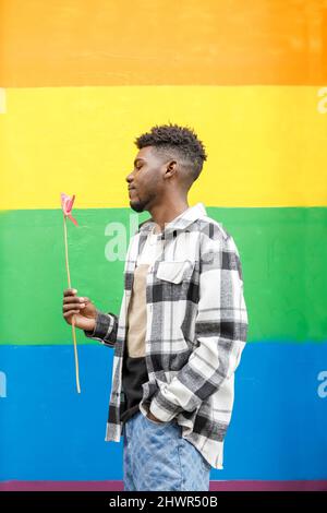 Young man with hand in pocket looking at flamingo lily in front of multi colored wall Stock Photo
