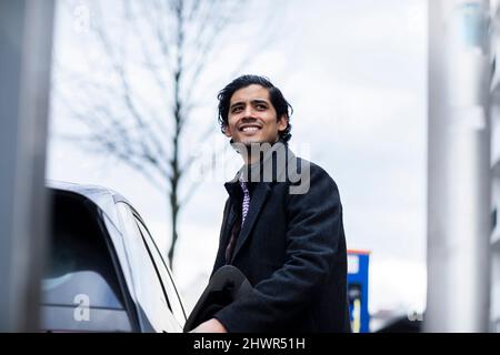 Happy man in warm clothing standing by car Stock Photo