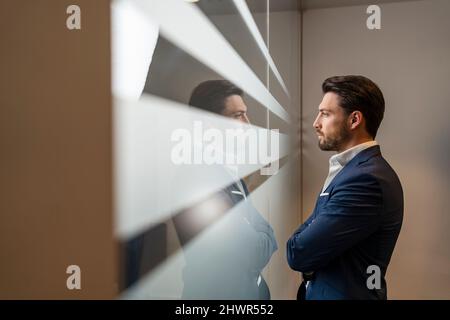 Confident businessman looking through window in office Stock Photo
