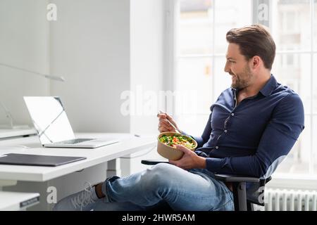 Businessman with salad bowl watching laptop at desk in office Stock Photo