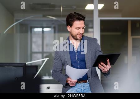 Businessman with document using tablet PC in office Stock Photo