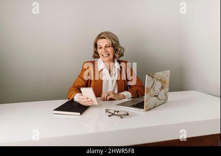 Happy businesswoman surfing net through smart phone at desk Stock Photo