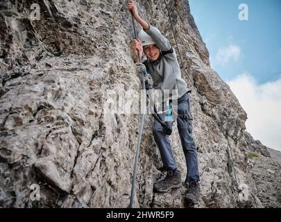 Smiling boy holding rope on rocky mountain Stock Photo