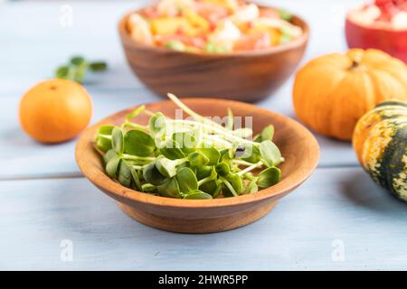 sunflower microgreen sprouts and vegetarian fruit salad of pumpkin, tangerine, pomegranate, grapefruit on blue wooden background. Side view, close up, Stock Photo