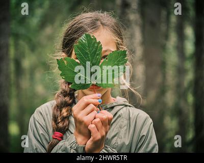 Girl covering face with maple leaf in forest Stock Photo - Alamy