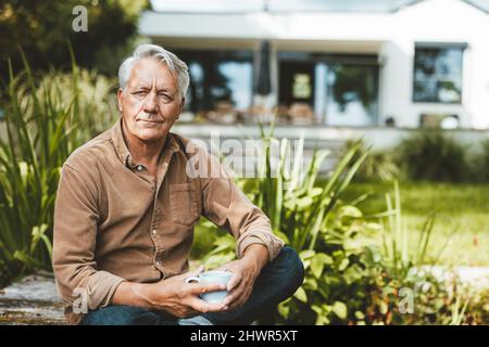 Thoughtful senior man holding coffee cup sitting in garden Stock Photo