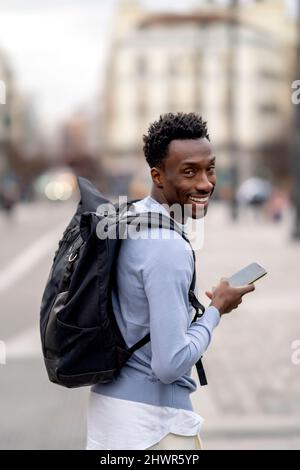 Smiling young man with backpack holding mobile phone Stock Photo