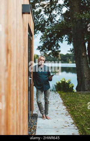 Senior man with hand in pocket holding tablet PC at backyard Stock Photo