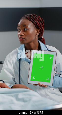 Medical specialist vertically holding green screen on tablet in hospital ward. Physician and sick person looking at gadget display with chroma key and isolated mockup background. Stock Photo