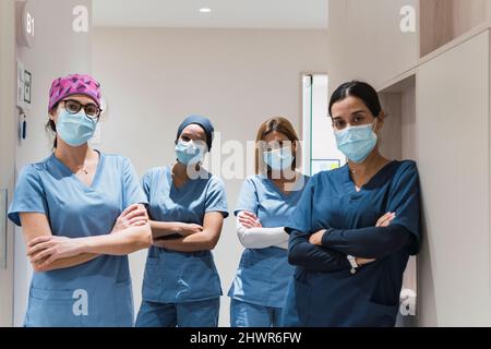 Doctors wearing protective face masks standing with arms crossed in corridor at hospital Stock Photo