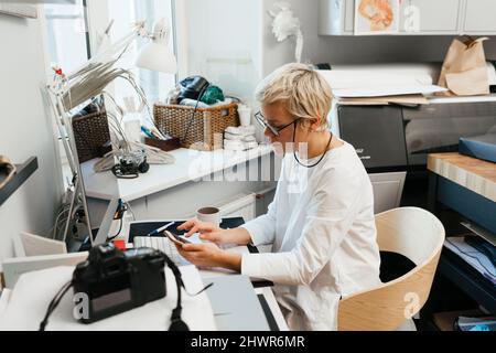 Woman using mobile phone sitting on chair at workplace Stock Photo