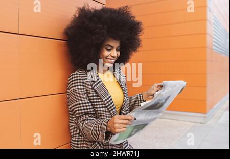 Smiling woman reading newspaper on footpath Stock Photo